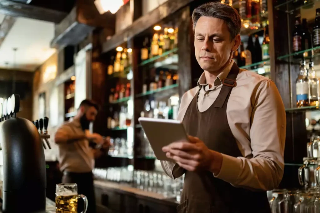Un responsable de restaurant consulte sa tablette numérique au bar pour vérifier la disponibilité des produits sur sa carte active.