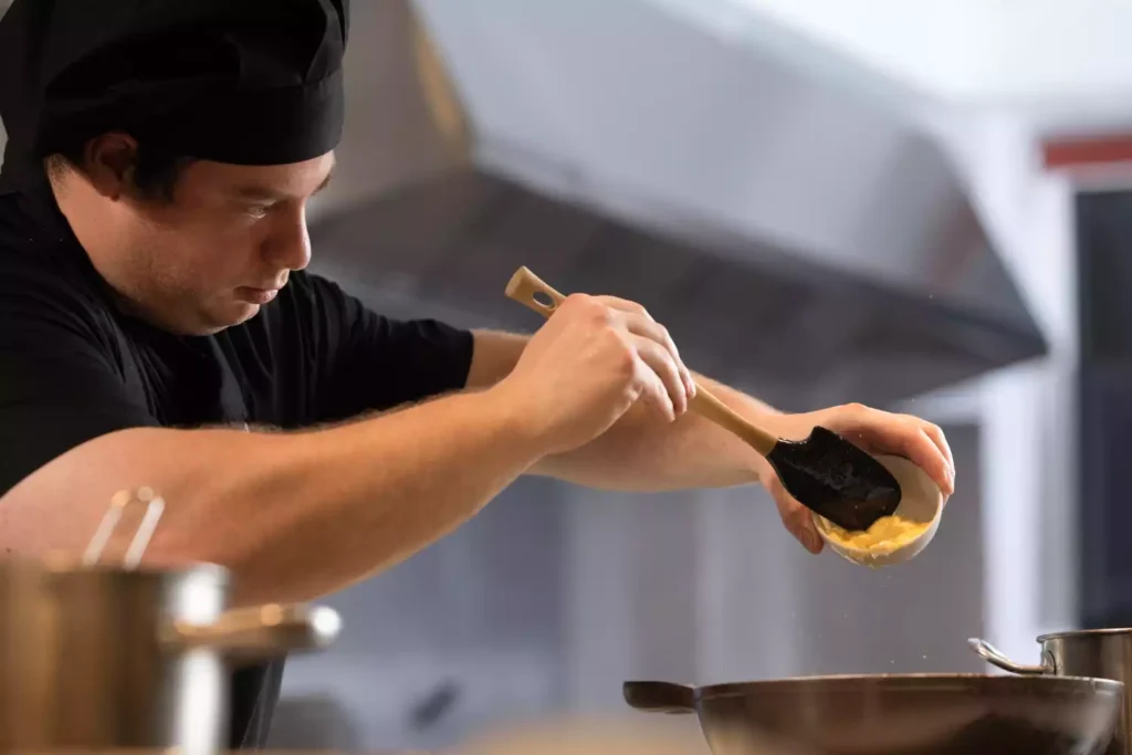 Chef en cuisine préparant activement le service, illustrant le début de la production alimentaire.